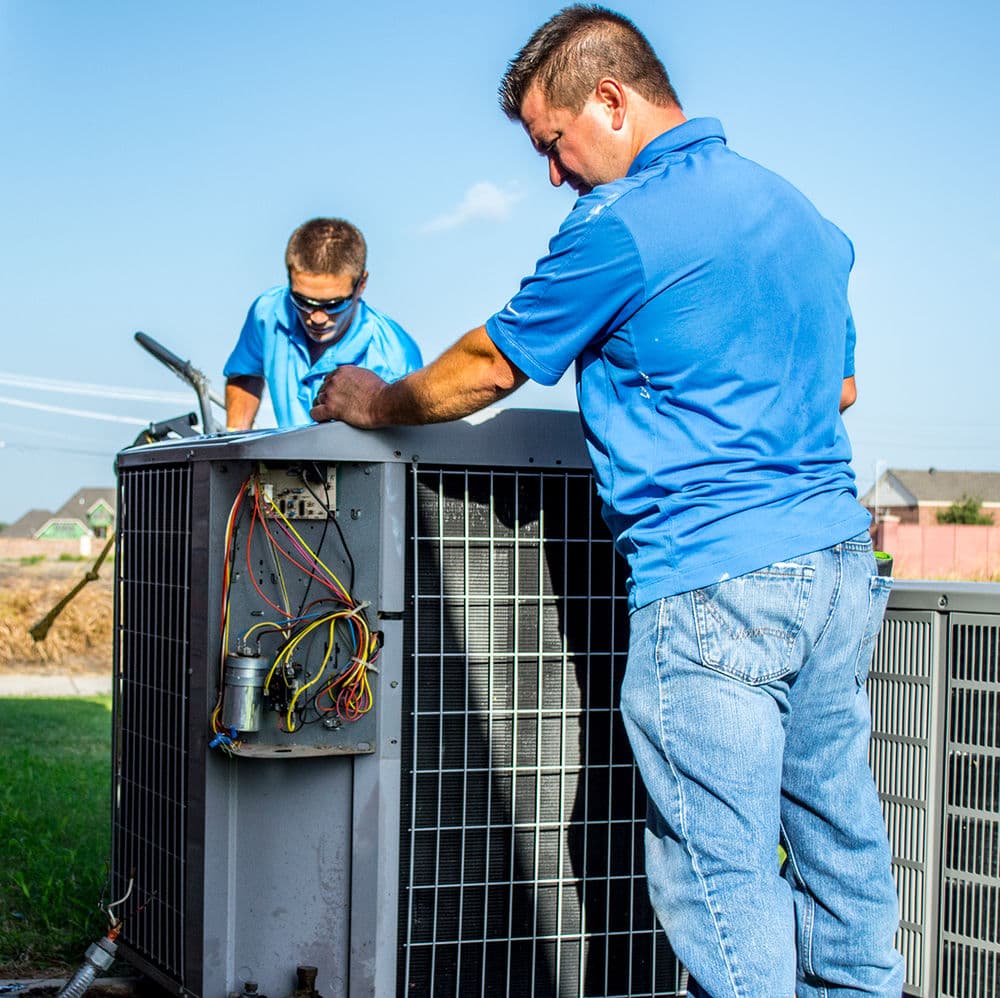 Technicians servicing an outdoor air conditioning unit in sunny residential setting.