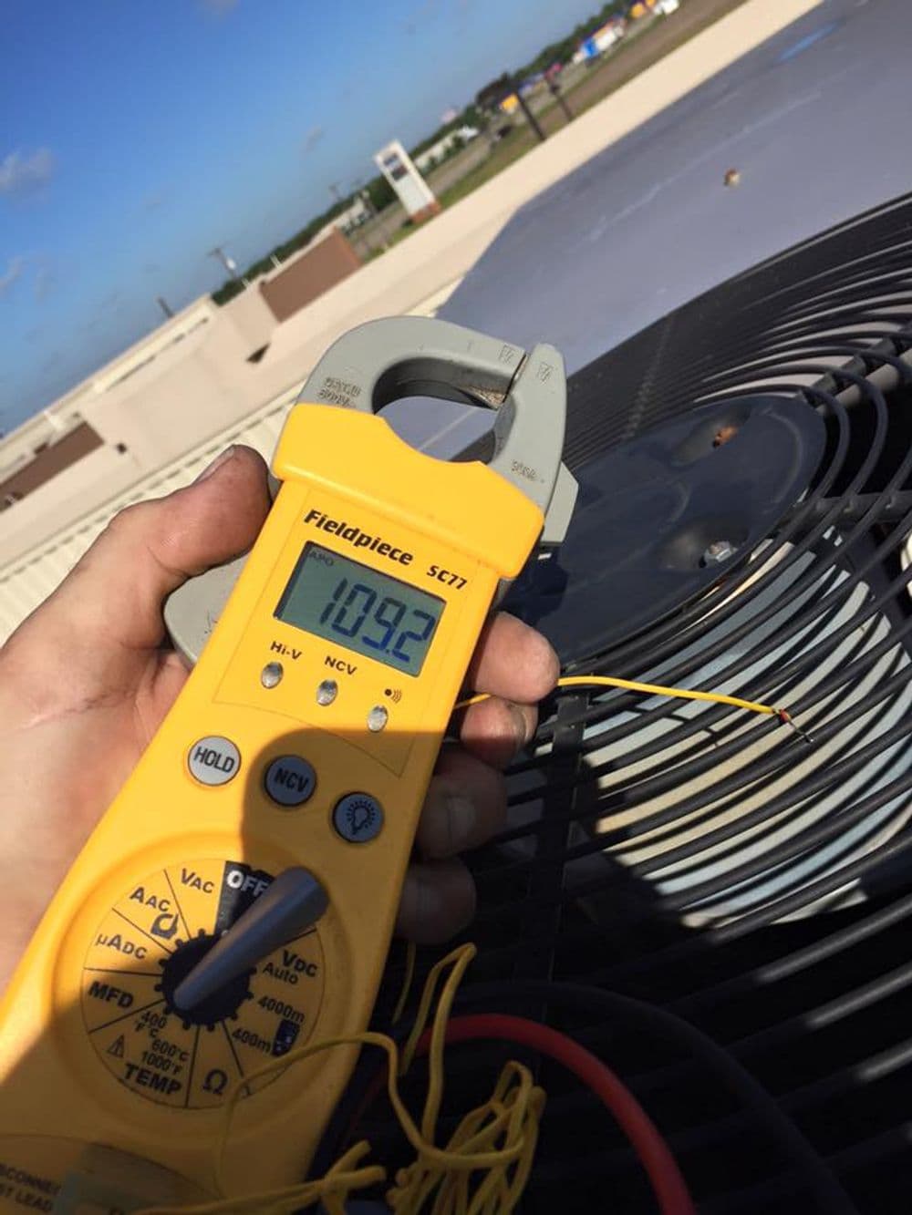 Technician using Fieldpiece SCT1 measuring instrument on HVAC system's rooftop.