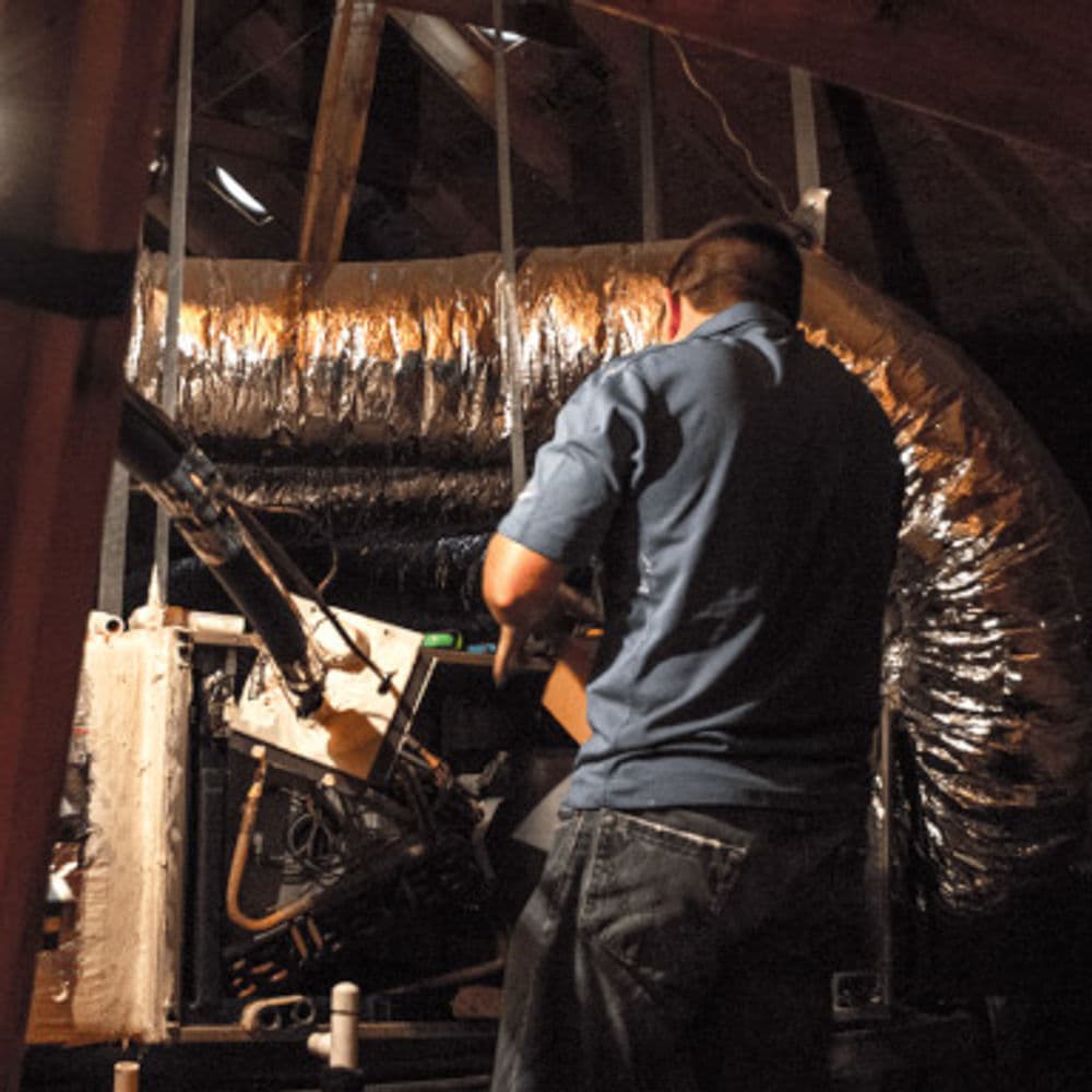 Man inspecting HVAC system in an attic, highlighting ductwork and equipment.