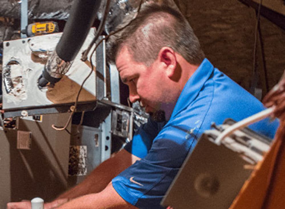 Technician repairing HVAC system in home attic, focused on equipment maintenance.